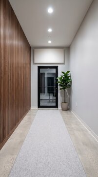 Quiet office entrance corridor with walnut slat wall, glass door, gray runner carpet and blank sign
