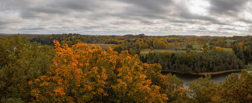 Panoramic autumn countryside with colorful forest, river and rolling fields under dramatic clouds