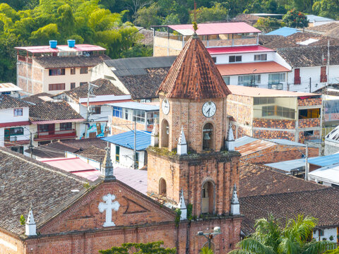Aerial view of the historic brick church in San Agustin, featuring a bell tower with clocks, surrounded by traditional houses with tiled roofs in San Agustin, Huila, Colombia.