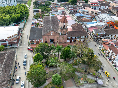 Aerial view of the San Agustin church and its surrounding plaza, featuring red-tiled roofs, lush green trees, and urban streets in San Agustin, Huila, Colombia.
