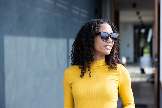African American woman posing near textured gray wall, wearing shades, yellow top at recessed entry