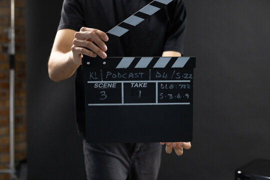 African American man wearing black tee and dark jeans holding clapperboard KL Podcast on studio set
