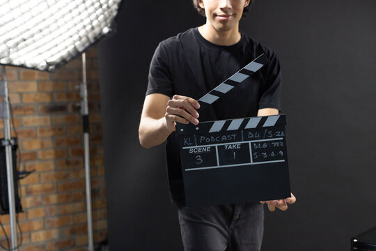 African American man wearing black tee, dark jeans holding slate marked KLI PODCAST in studio