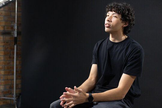 African American man sitting on stool in studio with black backdrop, wearing smartwatch, gazing up
