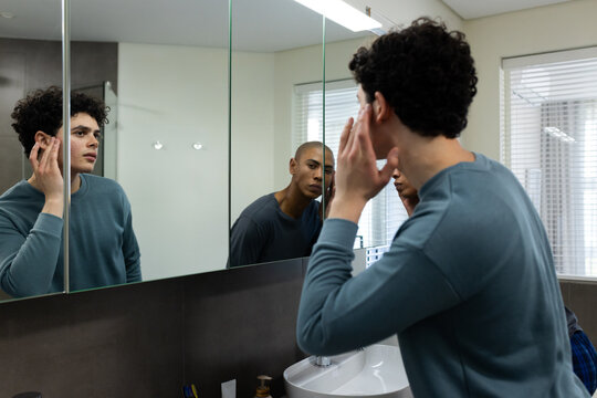African American men standing at bathroom sink, foreground wearing teal top touching ear in mirror