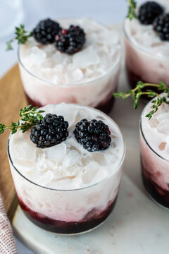 Blackberry and coconut milk drink with blackberry and thyme garnish on a marble and wood cutting board on a light surface 