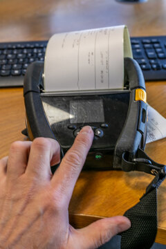 Close-up of a person pressing a button on a portable mobile direct thermal printer used for printing receipts, labels and other documents on the go. The handheld device represents mobile printing tech