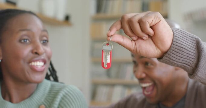 African American couple in green  and  brown sweaters reacting, man raising key on red tag, celebrat