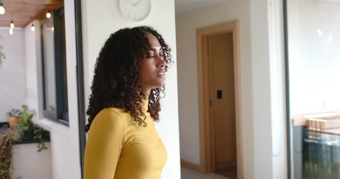 African American woman in mustard top at entry reacting to light at glass doors, turning, smiling