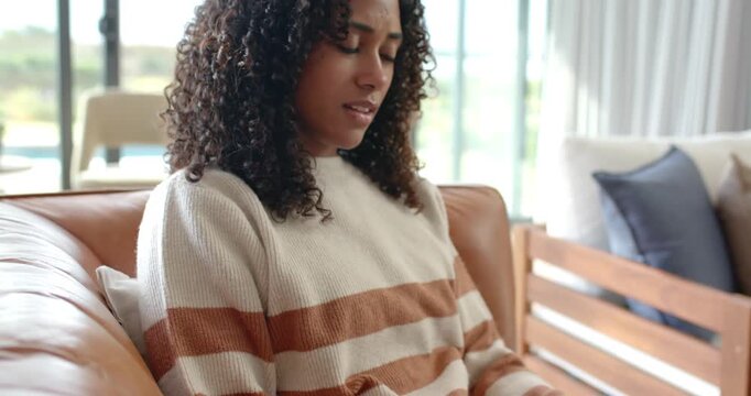 African American woman typing, pausing reading odd text, resuming typing on white laptop on couch