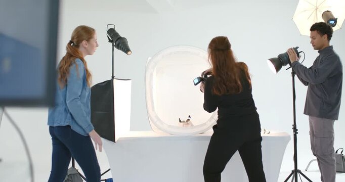 Crew approaching table using camera and tweaking strobe over light tent in studio for product shoot
