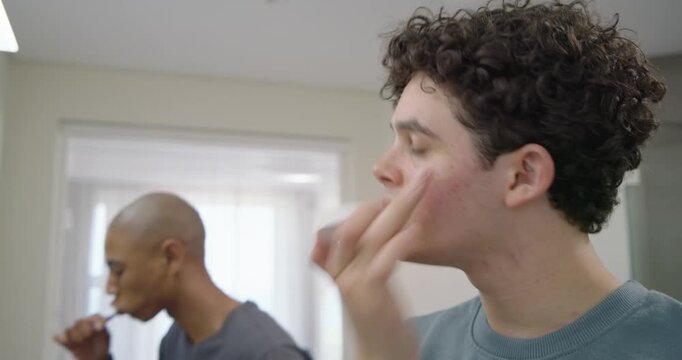 Two adult men prompted by morning routine squeezing toothpaste, brushing teeth at bathroom mirror