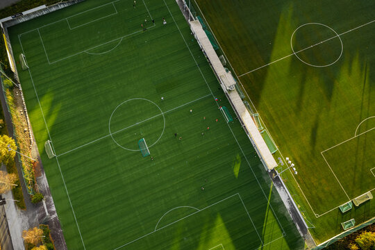 Aerial view of a football field with players training on the green turf, surrounded by trees and long shadows in Hommersak, Rogaland, Norway.
