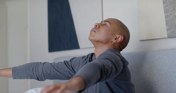 African American man waking to light, stretching on bed in blue plaid bottoms, smiling at bedmate