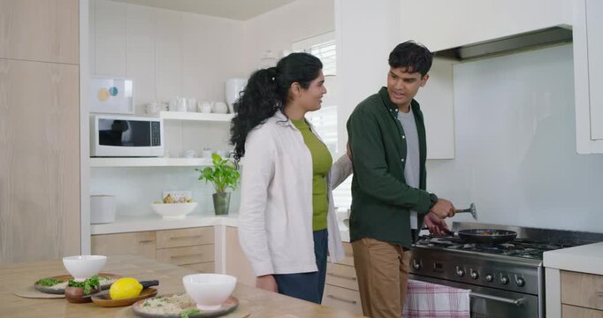 Indian couple bringing bowls to island, man plating food from pan with spatula onto plates serving