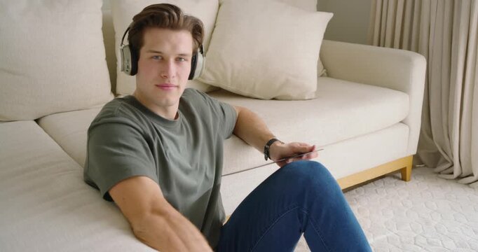 Adult male wearing headphones, hearing turntable playing, inspecting vinyl records on rug at home