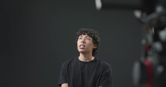 Man in his 20s responding to off-frame question in studio, looking up, gesturing at camera rig