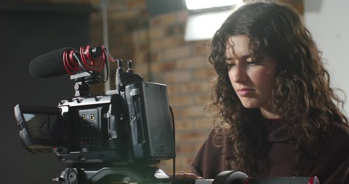 Female camera operator leaning, checking camera monitor, watching playback, testing setup in studio