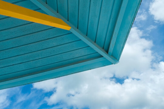 Aqua blue wooden palapa roof underside with yellow beam against cloudy sky