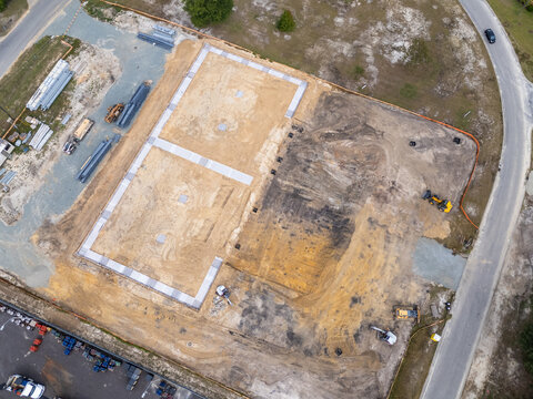 Aerial view of a construction site featuring a concrete building foundation, earthworks, and heavy machinery in Leland, North Carolina, United States.