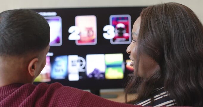 African American couple on couch, woman in striped top pointing to Top 10 on television, choosing