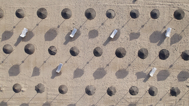 Aerial view of rows of straw parasols and white sun loungers on the sandy beach of Monte Gordo, Faro District, Portugal.