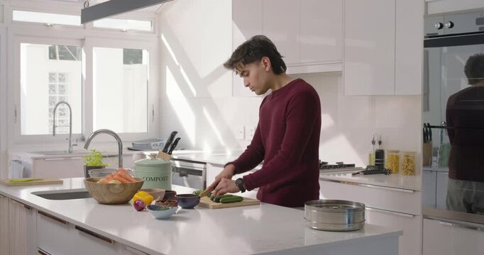 African man placing cucumber on board slicing with knife at island making salad, compost
