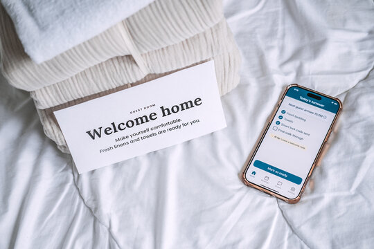 Welcome home card on linen stack beside host checklist phone. Welcome home card, guest welcome note, warm welcome, hospitality welcome