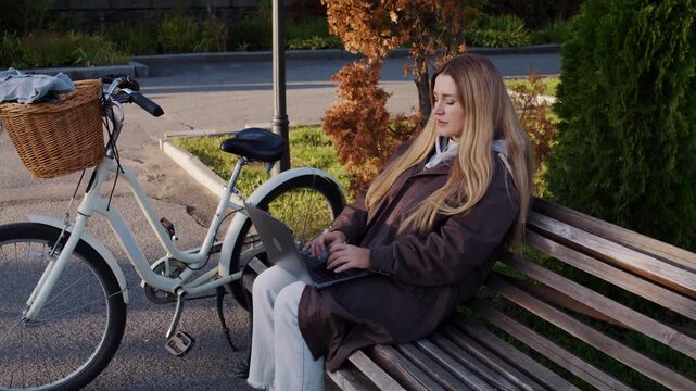 Woman student uses laptop to study as spends time in autumn park