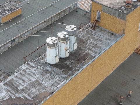 Aerial view of industrial rooftops with three large cylindrical storage tanks, metal piping, and brick building structures in Melbourne, Victoria, Australia.