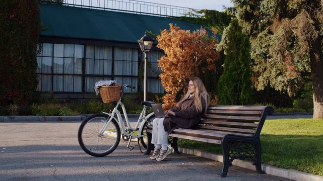 Young woman freelancer with laptop and bicycle in autumn park