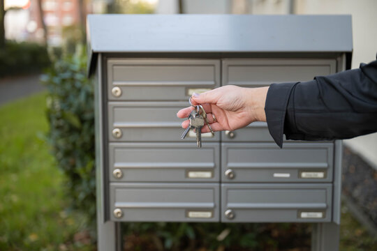 Hand holding several metal keys in front of residential mailboxes. Home access, property ownership, and the everyday task of collecting personal mail.