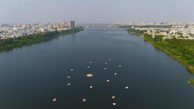 Aerial view of the Tapi River flowing through the city of Surat, with small circular structures floating on the water and urban buildings along the banks in Surat, Gujarat, India.