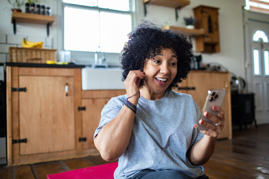Smiling woman putting in earbud while using smartphone at home