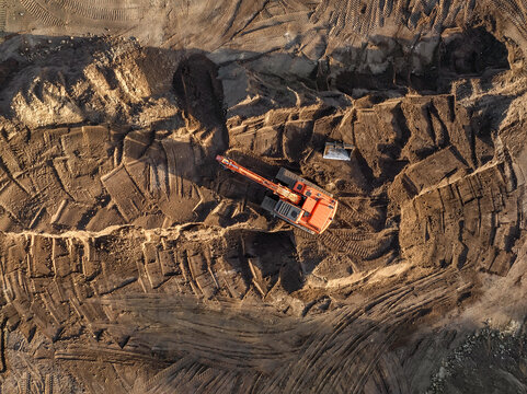 Aerial view of an orange excavator working on a construction site with brown soil and deep tire tracks in Enschede, Overijssel, Netherlands.