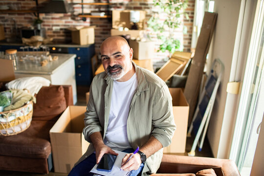 Smiling man writing moving checklist at home