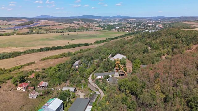 Drone view of the historic Tiribesi-Akna coal mine headframe amid summer forest and farmland near B&aacute;tonyterenye, Hungary, with the M&aacute;tra hills beyond.