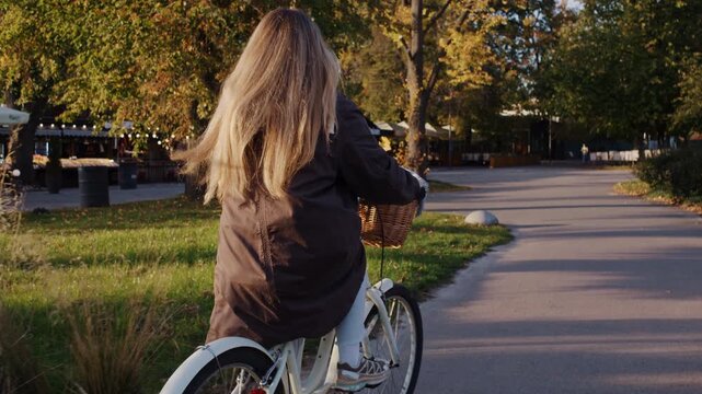 Woman with long loose hair rides bicycle along autumn park road
