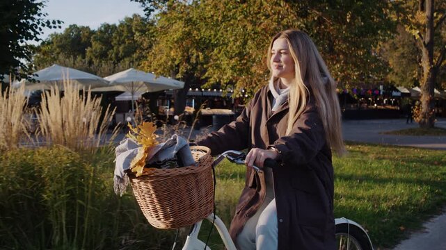 Happy blonde lady with blanket and leaves in basket rides bicycle
