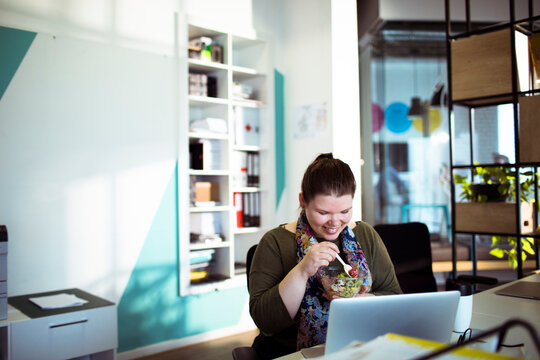 Smiling woman eating salad at office desk