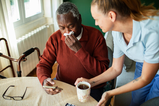 Caregiver offering tea to sick senior man at home