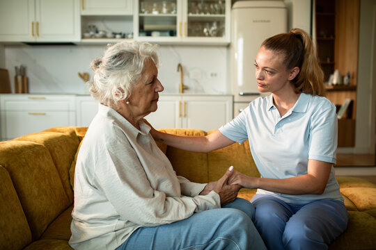 Caregiver comforting elderly woman at home on the sofa