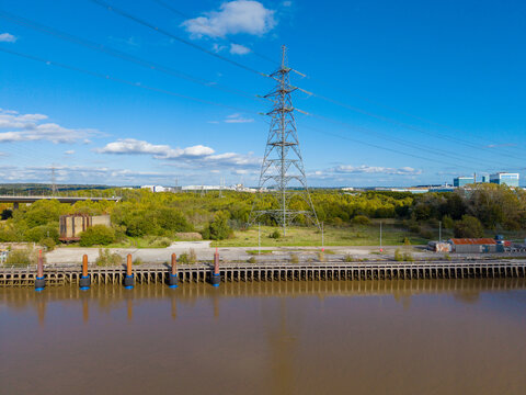 Deeside, United Kingdom - 11 October 2026: Aerial view of a large electricity pylon near the River Dee, with industrial buildings and trees in the background under a blue sky.