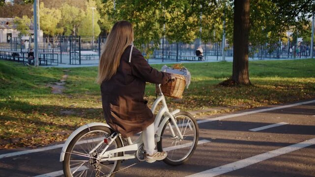 Long-haired blonde woman rides bicycle along track in autumn city