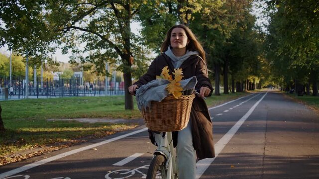 Woman in casual attire rides bicycle with basket in autumn park