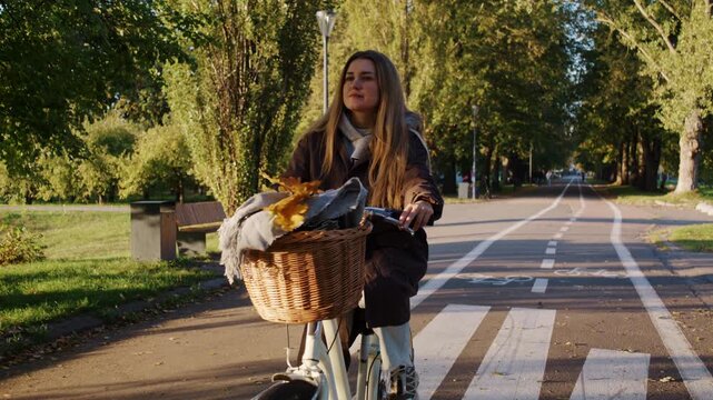 Pretty woman with loose hair rides bicycle through autumn park