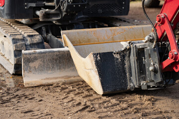 Wide excavator grading bucket hangs beside rubber crawler tracks and a front dozer blade, showing hydraulic earthmoving attachments used to level soil on construction sites © K