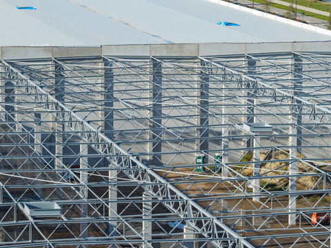 Genk, Belgium - 12 October 2026: Aerial view of the steel roof structure of a warehouse under construction, featuring concrete columns and industrial architecture in an expansion zone.