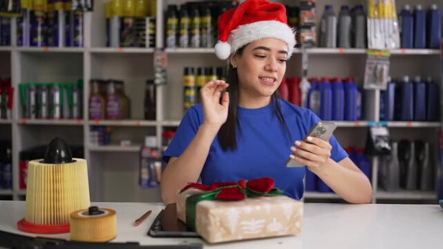 Happy latina woman wearing santa hat using smartphone to shop for christmas gifts in an auto parts store
