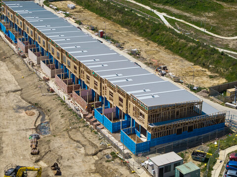 Melbourne, Australia - 08 October 2026: Aerial view of a residential construction site with a long row of townhouses under development, wooden framing, blue wrap, and metal roofing.